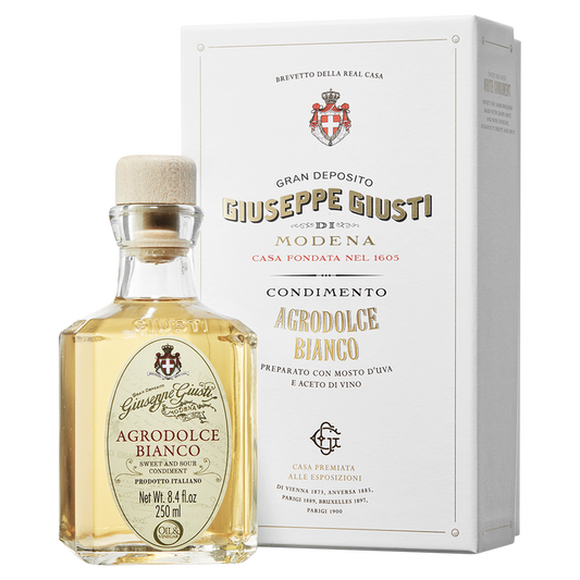 A bottle of Giuseppe Giusti Agrodolce Bianco di Modena balsamic vinegar next to its white gift box, both featuring the Giusti family crest.