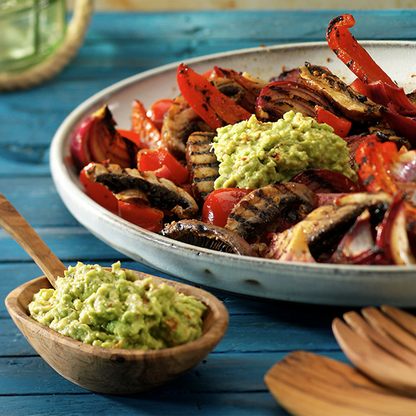 Bowl of guacamole and a plate with with roasted veggies on a blue wood table