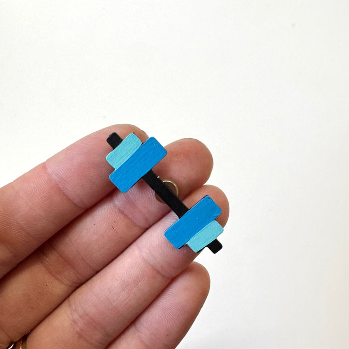 A close-up of a hand holding a small dumbbell-shaped magnet with bright blue and light blue rectangular weights on a black handle, against a plain white background.