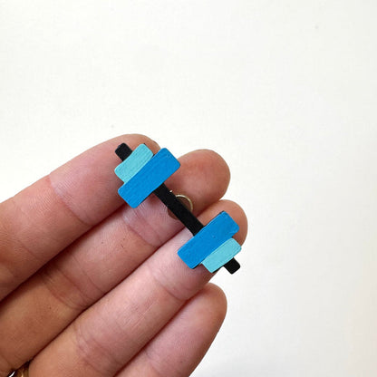 A close-up of a hand holding a small dumbbell-shaped magnet with bright blue and light blue rectangular weights on a black handle, against a plain white background.