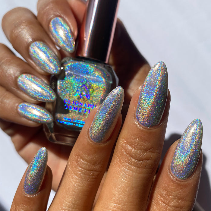 Close-up of nails painted with H₂Olo Nail Lacquer on medium skin tone. Hand is holding polish bottle.
