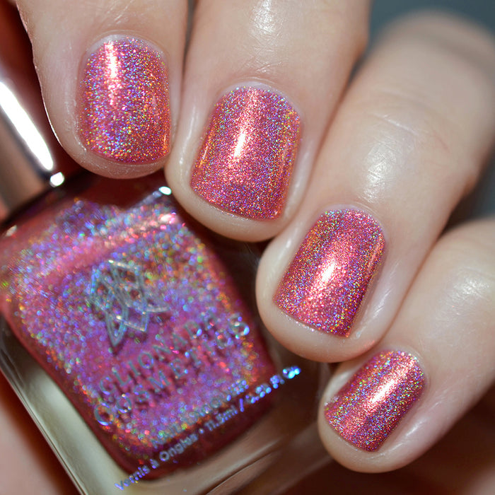 Close-up of nails painted with Flamin' Hot Holo Nail Lacquer on fair skin tone. Hand is holding polish bottle.