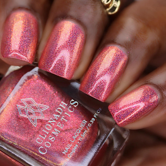 Close-up of nails painted with Flamin' Hot Holo Nail Lacquer on deep skin tone. Hand is holding polish bottle.