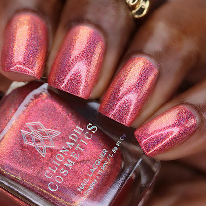 Close-up of nails painted with Flamin' Hot Holo Nail Lacquer on deep skin tone. Hand is holding polish bottle.