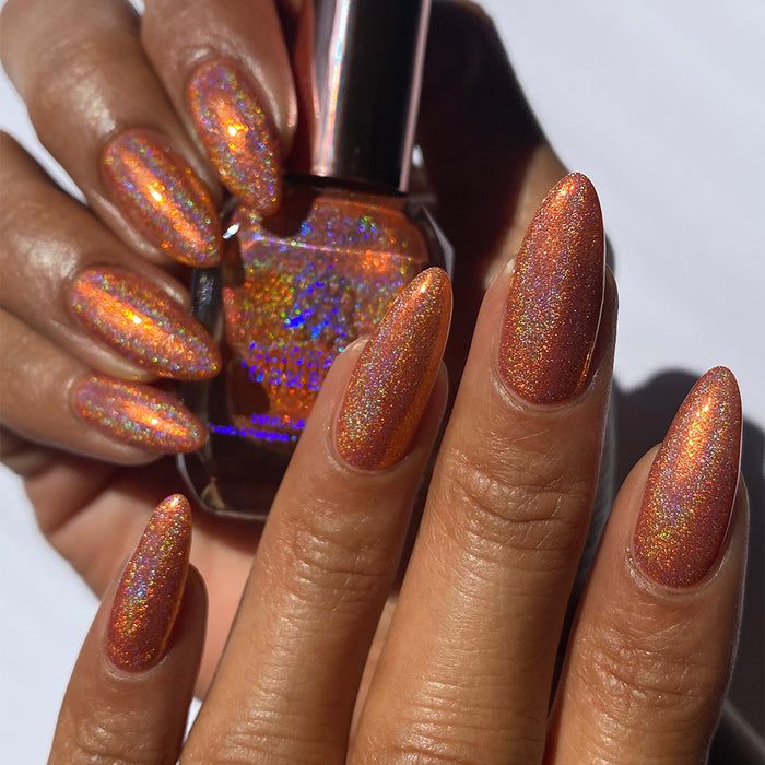 Close-up of nails painted with Holoritos Nail Lacquer on medium skin tone. Hand is holding polish bottle.