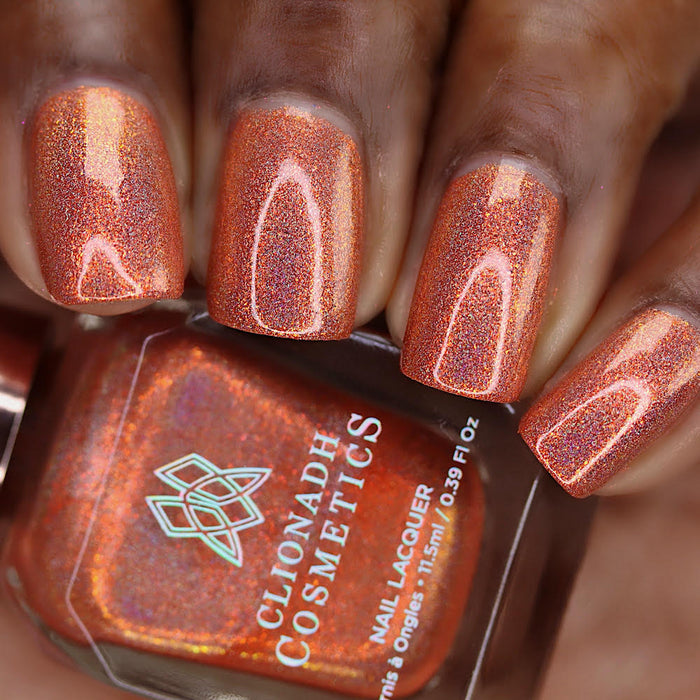 Close-up of nails painted with Holoritos Nail Lacquer on deep skin tone. Hand is holding polish bottle.