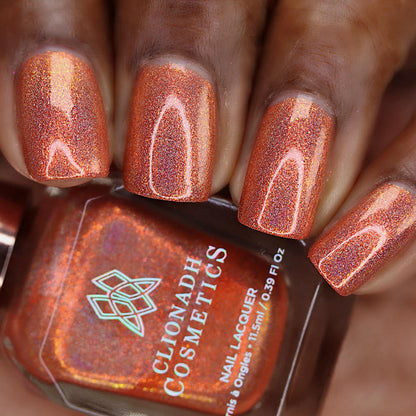 Close-up of nails painted with Holoritos Nail Lacquer on deep skin tone. Hand is holding polish bottle.