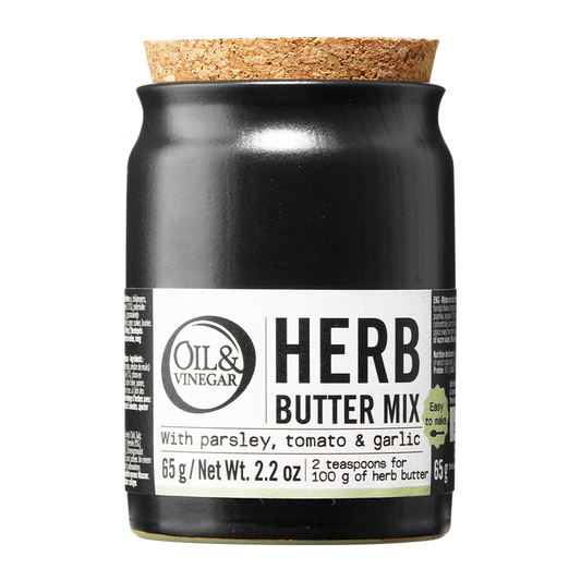 A jar of Herb Butter Mix by Oil & Vinegar with labels indicating the mix contains parsley, tomato, and garlic. The jar is sealed with a cork stopper.