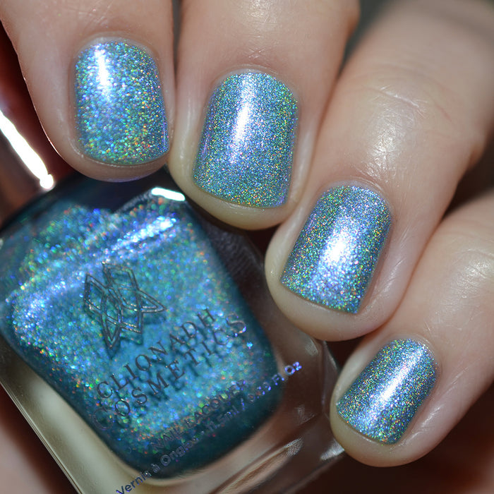 Close-up of nails painted with Holoberry Pie Nail Lacquer on fair skin tone. Hand is holding polish bottle.