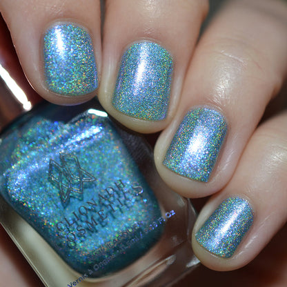 Close-up of nails painted with Holoberry Pie Nail Lacquer on fair skin tone. Hand is holding polish bottle.