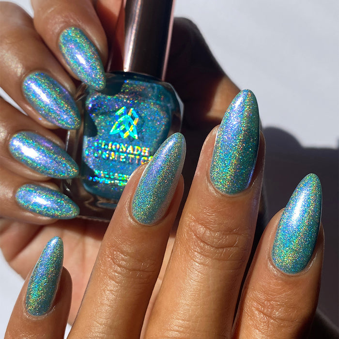 Close-up of nails painted with Holoberry Pie Nail Lacquer on medium skin tone. Hand is holding polish bottle.