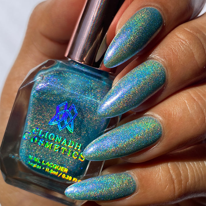 Close-up of nails painted with Holoberry Pie Nail Lacquer on medium skin tone. Hand is holding polish bottle.