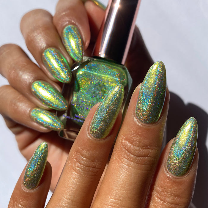 Close-up of nails painted with Holondaise Nail Lacquer on medium skin tone. Hand is holding polish bottle.