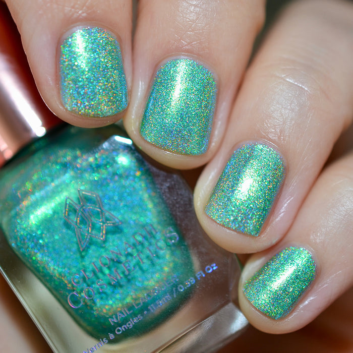 Close-up of nails painted with Holopeño Nail Lacquer on fair skin tone. Hand is holding polish bottle.
