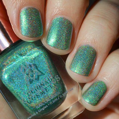 Close-up of nails painted with Holopeño Nail Lacquer on fair skin tone. Hand is holding polish bottle.