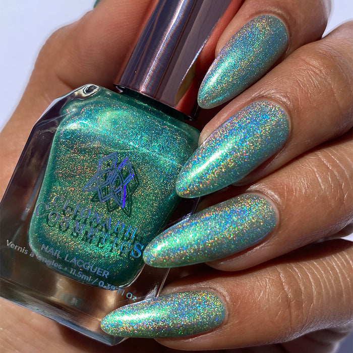 Close-up of nails painted with Holopeño Nail Lacquer on medium skin tone. Hand is holding polish bottle.
