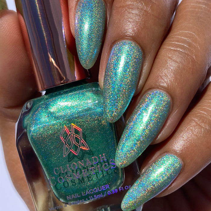 Close-up of nails painted with Holopeño Nail Lacquer on medium skin tone. Hand is holding polish bottle.