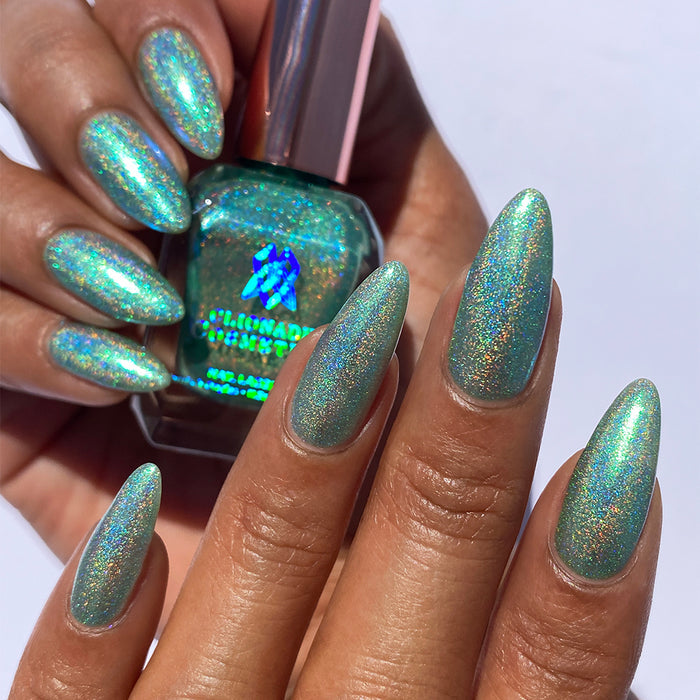 Close-up of nails painted with Holopeño Nail Lacquer on medium skin tone. Hand is holding polish bottle.