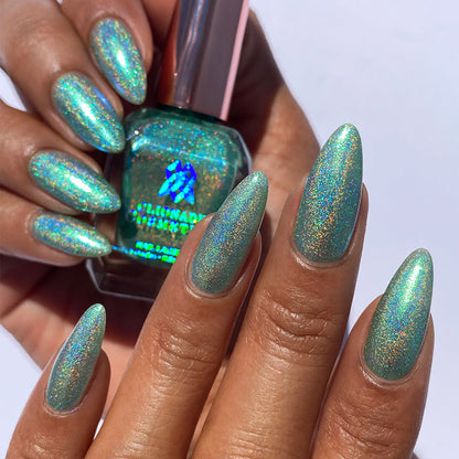 Close-up of nails painted with Holopeño Nail Lacquer on medium skin tone. Hand is holding polish bottle.