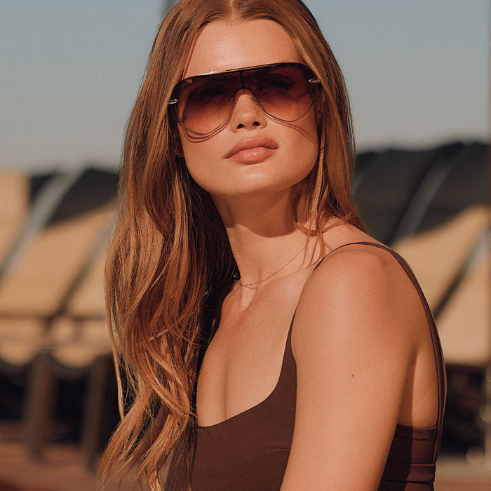 lifestye - female at the beach wearing diff eyewear featuring the imani shield sunglasses with a gold frame and brown gradient lenses front view