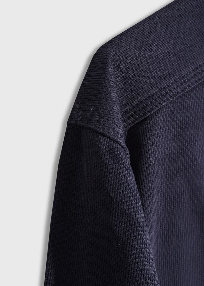 Close-up of a navy blue textured fabric on a garment, showing detailed stitching and ribbed pattern against a light gray background.