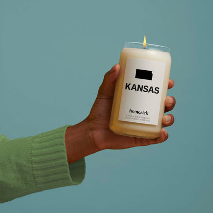 A hand holding the Kansas candle over a blueish green background.