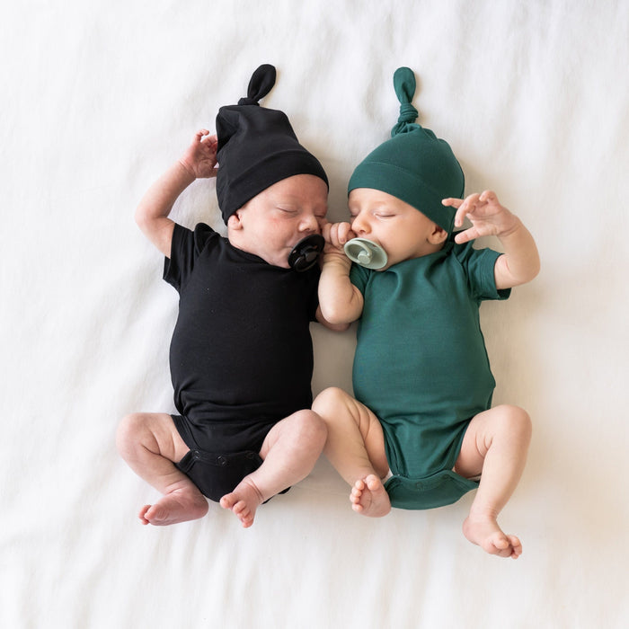 Newborns sleeping next to each other while wearing  Knotted Caps and matching Short Sleeve Bodysuits in Midnight and Emerald