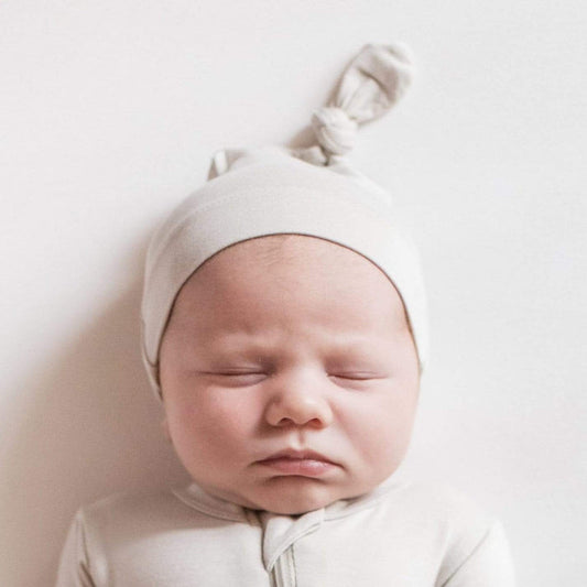 Sleeping newborn wearing a Kyte Baby Knotted Cap in Oat