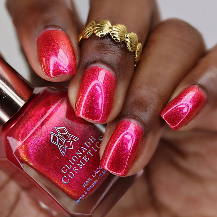 Close-up of nails painted with La Vie En Rose Nail Lacquer on deep skin tone. Hand is holding polish bottle.