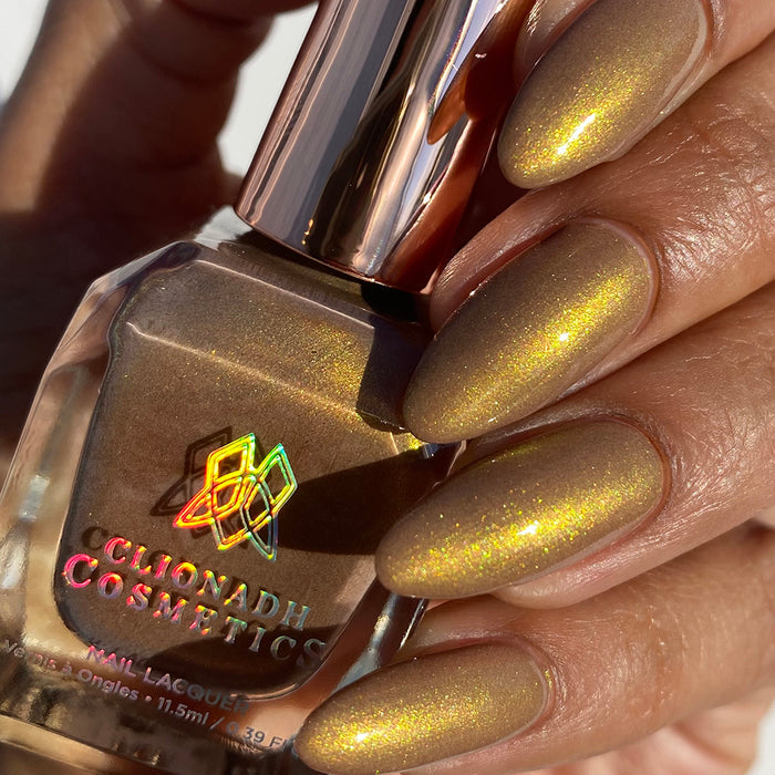Close-up of nails painted with Lattes and Ciders Nail Lacquer on medium skin tone. Hand is holding polish bottle.