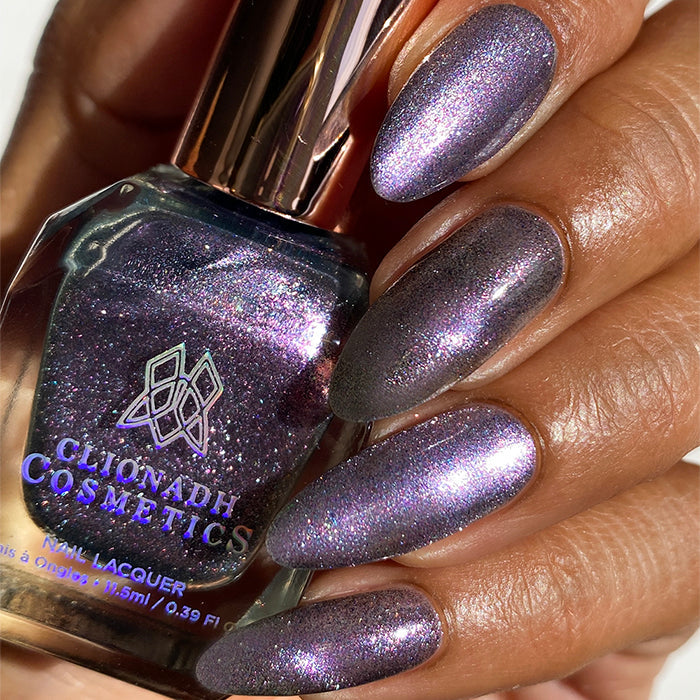 Close-up of nails painted with Lilac Velour Nail Lacquer on medium skin tone. Hand is holding polish bottle.