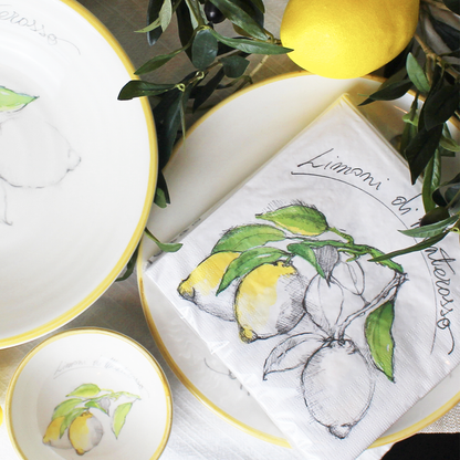 Limoni napkins on yellow and white plates on a table scape with a whole lemon and greenery as decor