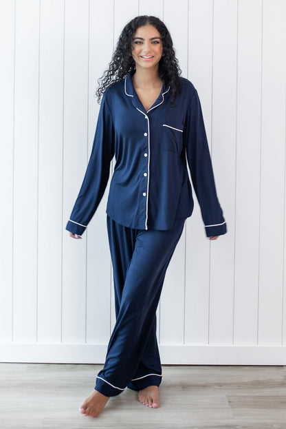 Female standing in front of a white paneled wall wearing the Long-Sleeved Women's Pajama Set in Navy with Cloud Trim