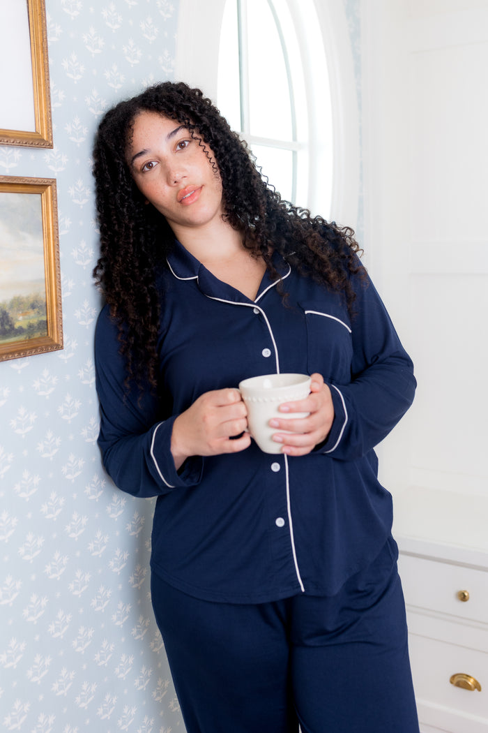 Female wearing the Long-Sleeved Women's Pajama Set in Navy with Cloud Trim leaning his friend against a wall holding a white coffee cup