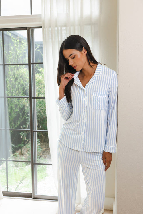 Female modeling the Long-Sleeved Women's Pajama Set in Small Mist Stripe with Cloud Trim leaning against a wall