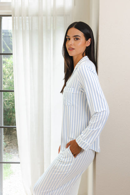 Female modeling the Long-Sleeved Women's Pajama Set in Small Mist Stripe with Cloud Trim leaning against a wall