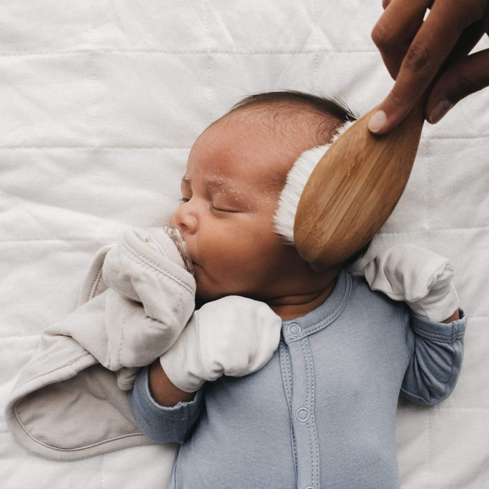 Sleeping newborn with Kyte Baby Lovey in Oat while wearing Scratch Mittens in Oat and Snap Footies in Fog