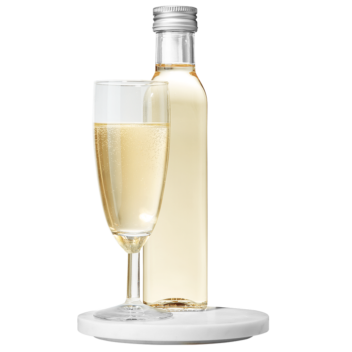A bottle of Marc de Champagne Vinegar placed next to a filled champagne flute, both resting on a white surface.