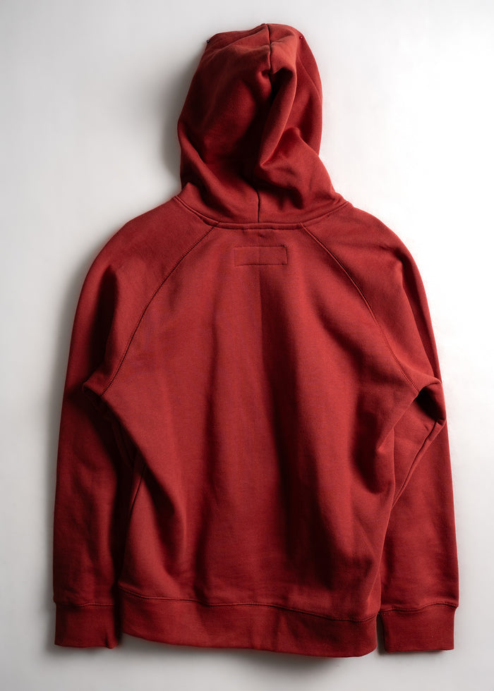 A red hoodie is laid flat on a light surface, showcasing its back design and hood, emphasizing its casual style and color.