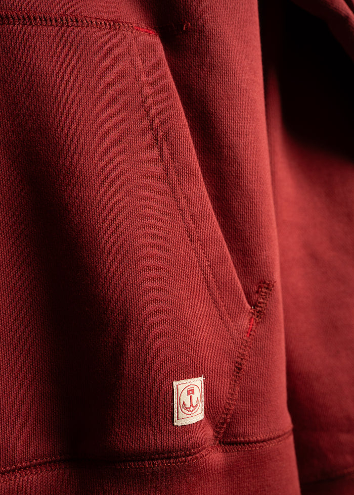 Close-up of a red hoodie pocket with a small anchor logo patch, highlighting the fabric texture and stitching details.