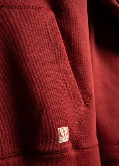 Close-up of a red hoodie pocket with a small anchor logo patch, highlighting the fabric texture and stitching details.