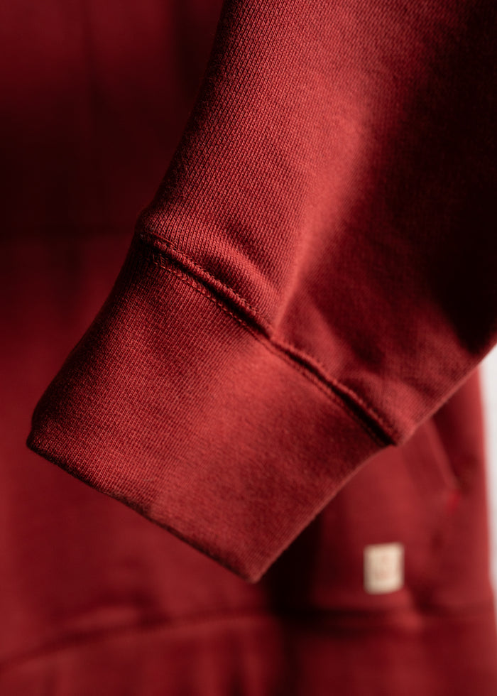 Close-up of a red sweatshirt sleeve, showcasing its soft fabric texture and ribbed cuff, with a small tag visible in the background.
