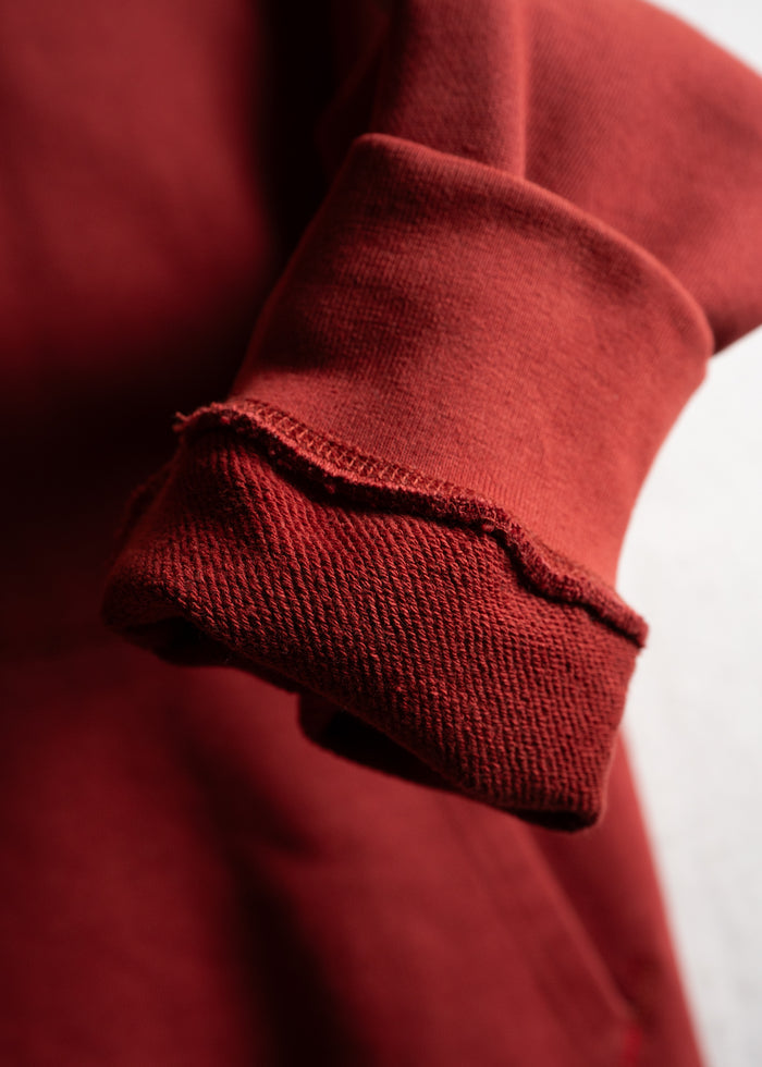 Close-up of a rolled-up red sweatshirt sleeve, highlighting the textured fabric and stitching details in soft lighting.