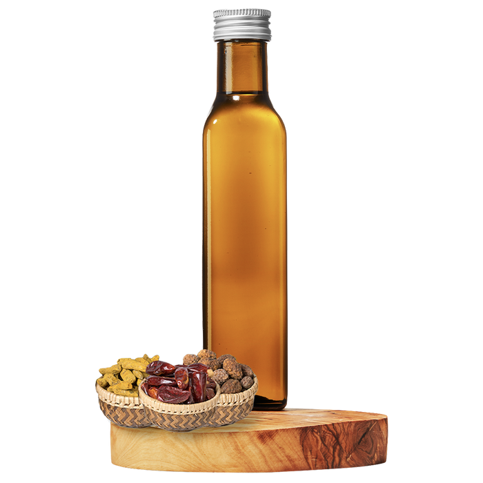A tall, clear amber bottle of grapeseed oil on a wooden platform, with a small basket of dried spices next to it.