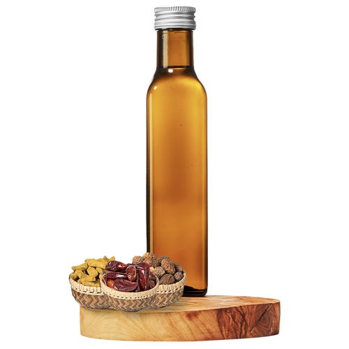 A tall, clear amber bottle of grapeseed oil on a wooden platform, with a small basket of dried spices next to it.