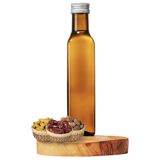 A tall, clear amber bottle of grapeseed oil on a wooden platform, with a small basket of dried spices next to it.