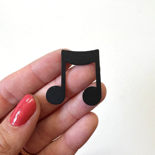 A hand with red nail polish holds a small black music note magnet against a plain white background.