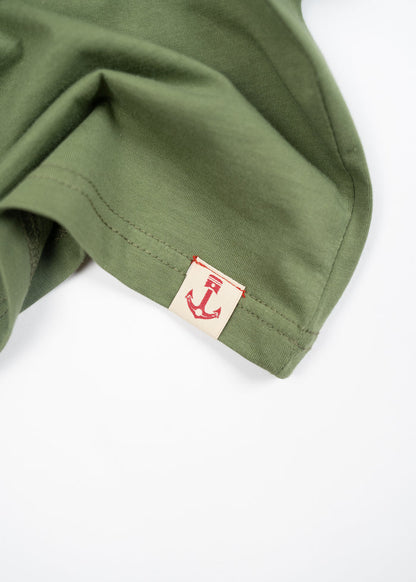 Green fabric with a red anchor tag on the edge, highlighting nautical design. The fabric is neatly folded, showing texture.