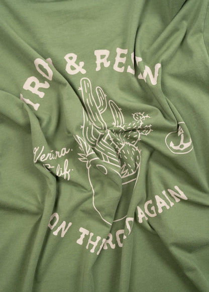 Green shirt with white cactus design and text reading "Iron & Resin, Ventura, Calif, On the Road Again" in a casual style.