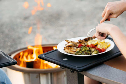 This is an image of someone eating grilled chicken on a Breeo Outrig Tray